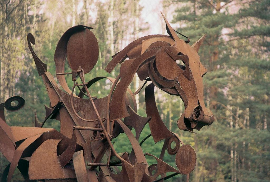 나무의 배경에 세워진 말의 머리의 녹슨 금속 조각.