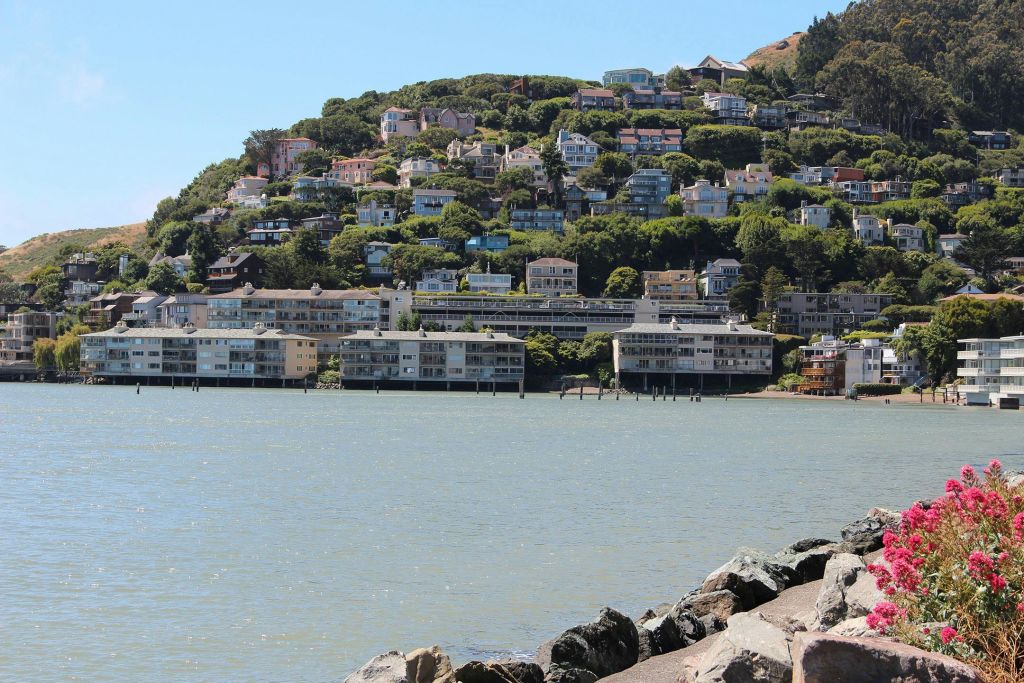 수많은 주택이 있는 언덕길에서는 잔잔한 물이 내려다보이고, 푸른 하늘 아래 전경에 바위가 늘어서 있습니다.