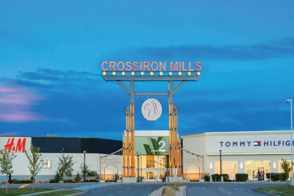황혼 하늘 아래 타미 힐피거를 비롯하여 커다란 표지판과 주변 상점이 있는 CrossIron Mills 쇼핑 센터 입구.