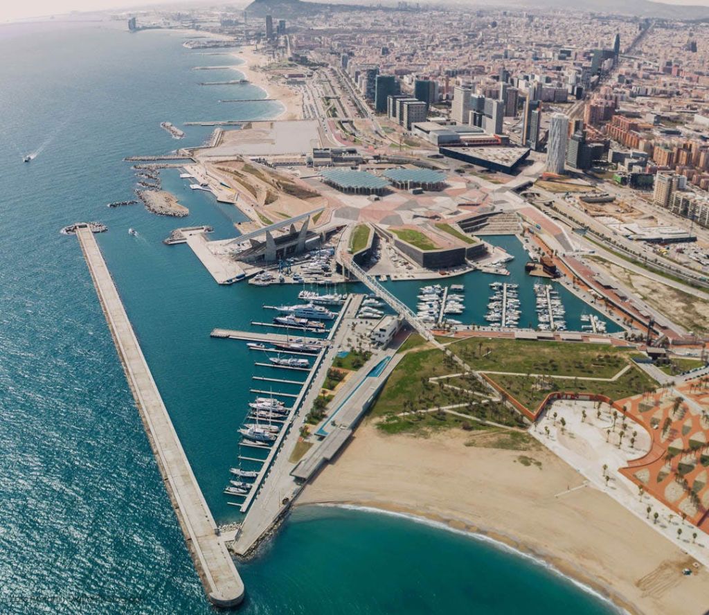 대형 워터프론트에 인접한 정박지, 보트, 해변, 수많은 건물이 있는 해안 도시의 공중 전망.