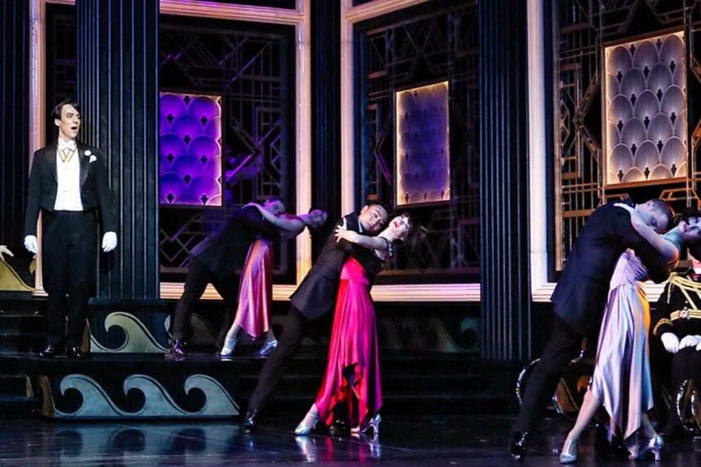 정장 차림의 배우들은 무대에서 예술적 감각에서 영감을 받은 세트와 다채로운 조명으로 드라마틱한 장면을 연출합니다.