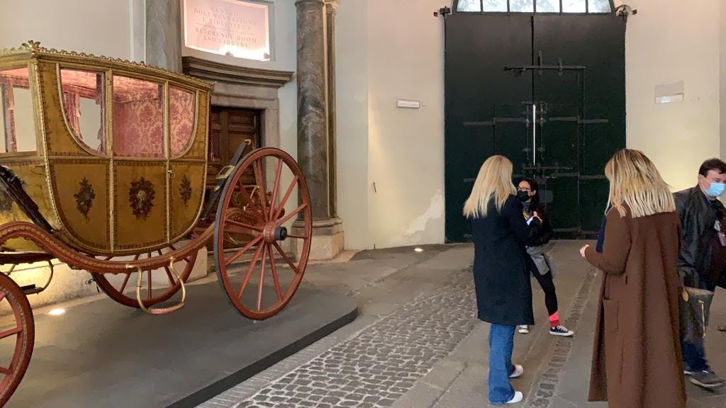 자갈 바닥이 있는 유서 깊은 건물에 커다란 나무 바퀴가 달린 앤티크 마차 근처에 서 있는 두 명의 여성.