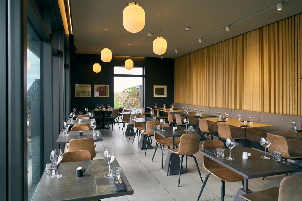 갈색 의자, 와인잔이 놓인 테이블, 커다란 창문, 나무 패널 벽, 행잉 글로브 조명이 있는 현대적인 레스토랑.