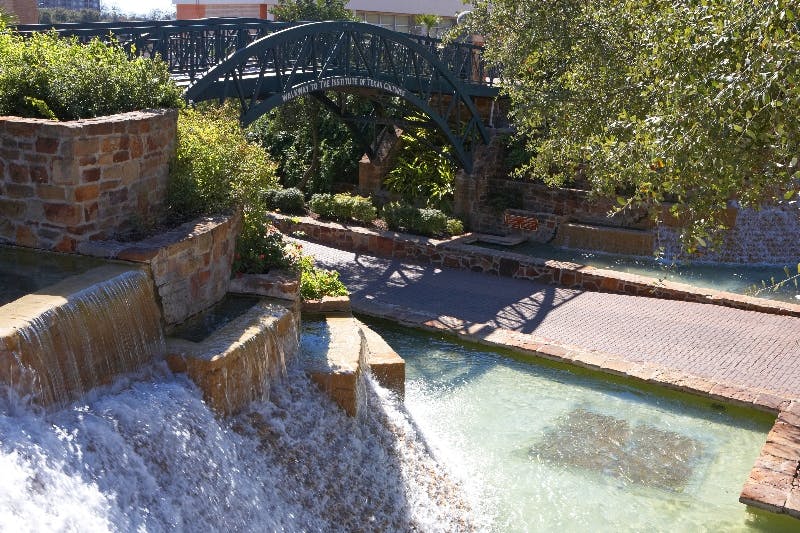 계단식 물, 돌길, 녹지, 장식용 아치형 다리를 배경으로 한 경치 좋은 공원입니다.