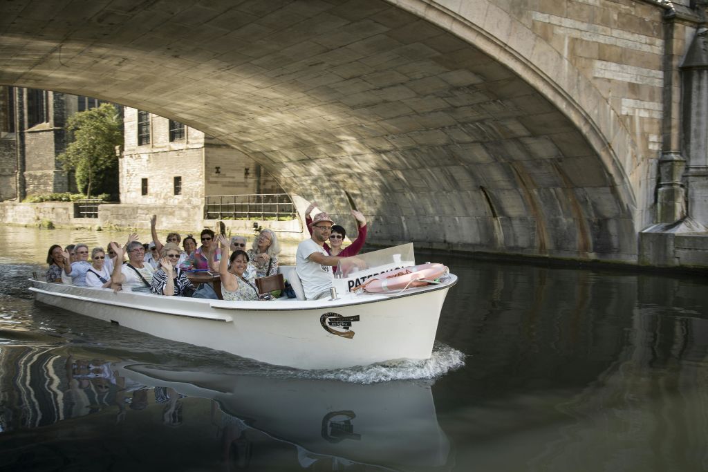 화창한 날 돌다리 아래에서 하얀 보트를 타며 한 무리의 사람들이 손을 흔들며 미소를 짓고 있습니다.