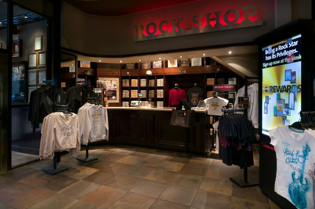 셔츠, 기념품, 의류 선반을 포함한 상품 진열대가 있는 "Rock Shop" 이라고 표시된 소매점의 내부.