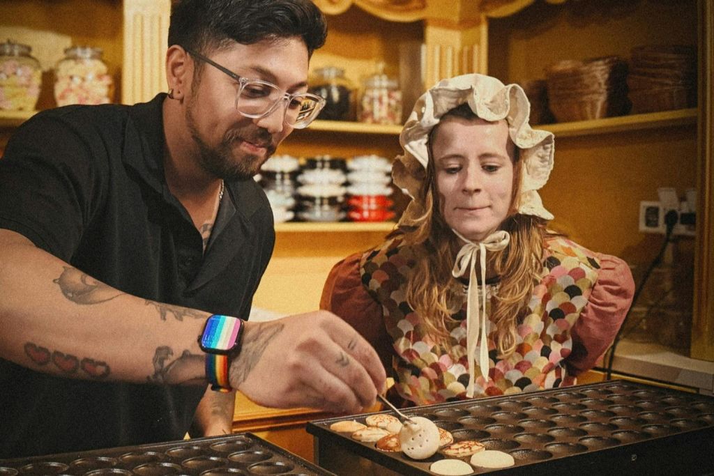 빈티지 주방에서 작은 페이스트리를 요리하는 두 사람. 하나는 무지개 손목 밴드를 착용하고 다른 하나는 전통적인 보닛을 착용합니다.