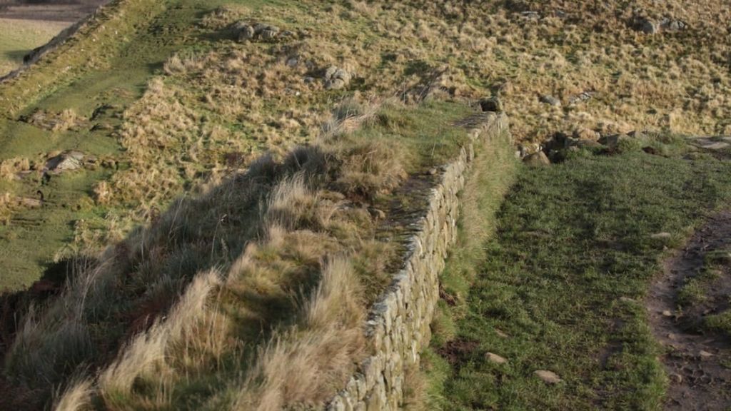 언덕이 우거진 잔디밭에 바위 덩어리와 희박한 초목이 우거진 잔디로 뒤덮인 고대의 돌담.