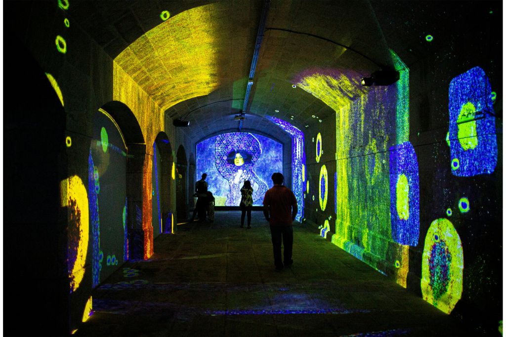 벽과 천장에 화려하고 추상적으로 투영된 조명이 켜진 터널을 거닐고 있습니다.