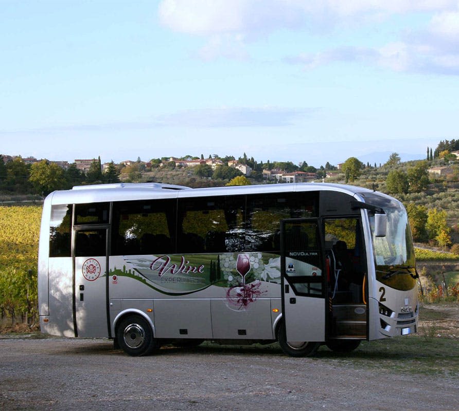 포도밭과 멀리 떨어진 마을이 있는 경치 좋은 시골에 주차된 "와인" 브랜딩이 있는 투어 버스.
