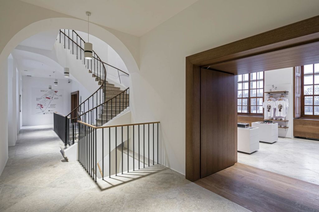 검은색 난간이 있는 계단, 커다란 창문이 있는 방으로 이어지는 열린 문, 조명 기구가 있는 내부 복도.