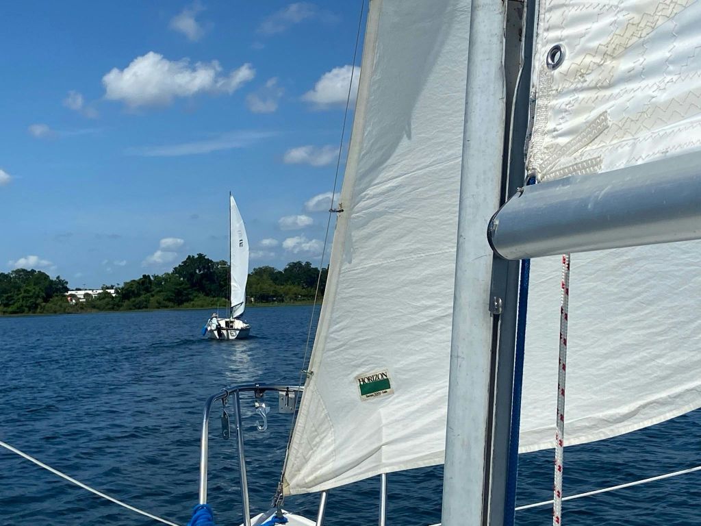 흰 구름과 함께 푸른 하늘 아래 잔잔한 물 위에서 요트를 타세요. 전경에는 요트 한 척, 저 멀리에는 요트 한 척이 있습니다.