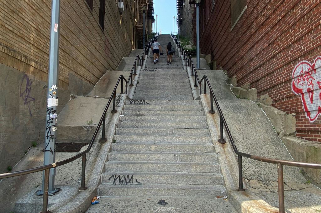 벽돌과 나무 벽을 사이에 두고 양쪽에 난간이 달린 긴 콘크리트 계단을 오르는 두 사람.