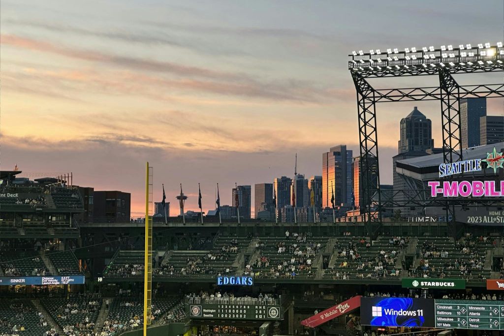 석양이 질 무렵 도시의 스카이라인을 조망할 수 있는 야구 경기장으로 스탠드, 스코어보드, 야전 조명탑이 있습니다.