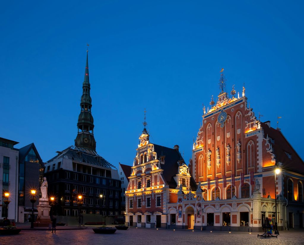 밝게 빛나는 고딕 양식의 건물과 깊고 푸른 하늘을 배경으로 높고 가느다란 첨탑이 있는 해질 무렵의 유서 깊은 광장입니다.