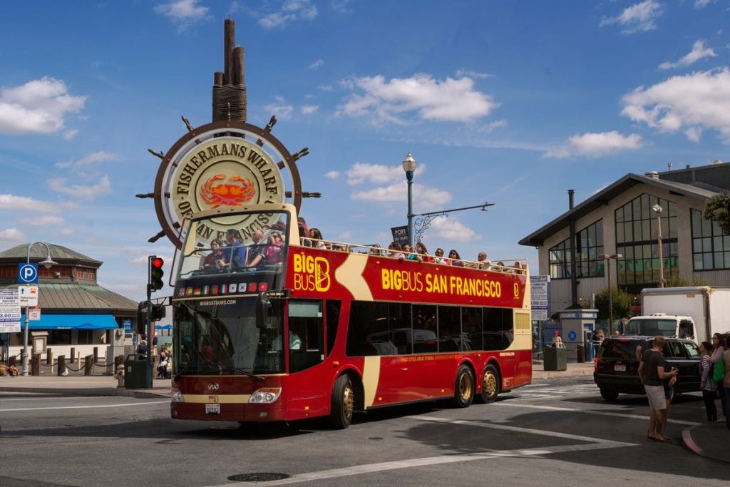 화창한 날 피셔맨스 워프 (Fisherman's Wharf) 표지판을 지나가는 '빅 버스 샌프란시스코 (Big Bus San Francisco)' 라는 이름의 2층 투어 버스.