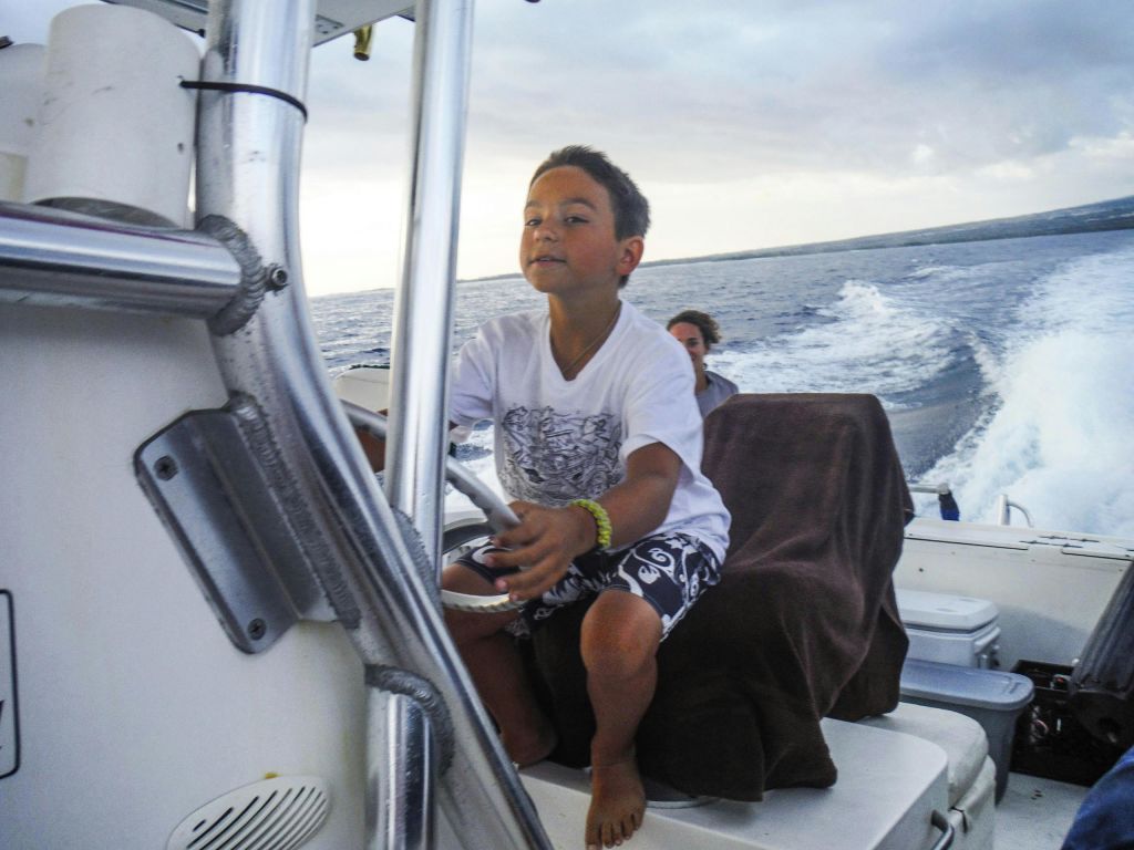 탁 트인 바다에서 보트를 조종하는 어린이가 근처에 앉아 있습니다. 배경은 바다와 흐린 하늘을 보여줍니다.