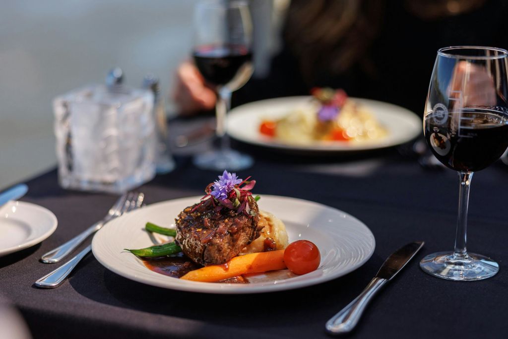 스테이크, 채소, 장식품을 흰색 접시에 담고 레드 와인 한 잔과 다른 요리를 곁들인 고급 요리입니다.