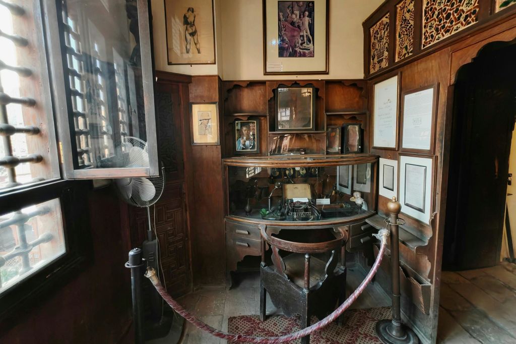 빨간 로프 장벽으로 둘러싸인 벽에 타자기, 액자 사진, 문서가 놓인 빈티지 목재 서재 책상.