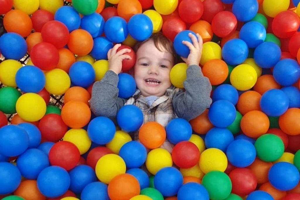 빨간색, 파란색, 노란색 및 녹색 플라스틱 공으로 둘러싸인 화려한 공 구덩이에서 웃고 누워있는 어린이.