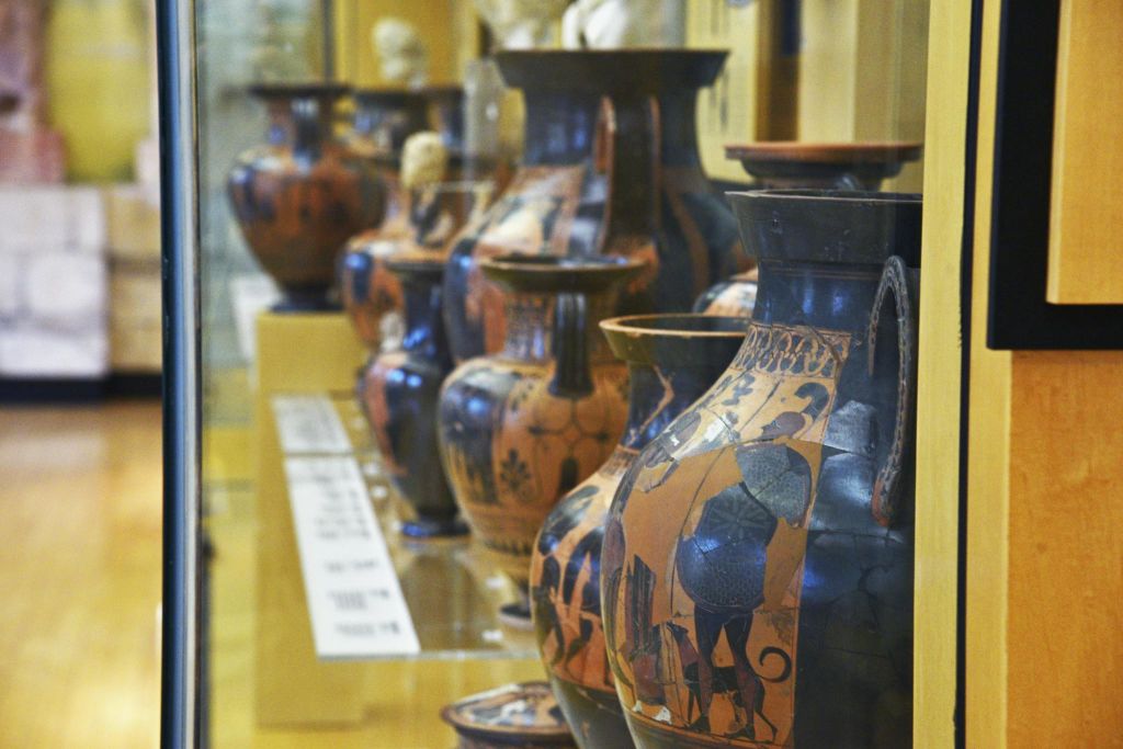 고대의 페인트 도자기 꽃병이 박물관에 전시되어 있으며, 정보용 플라크가 있는 선반에 배치되어 있습니다.