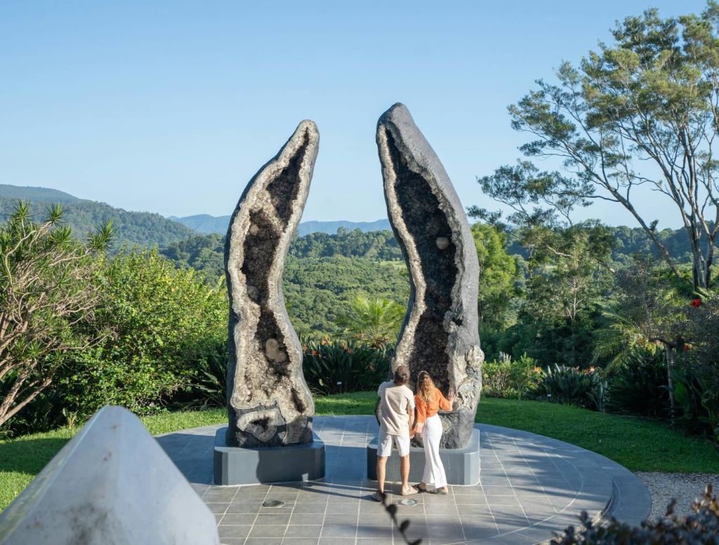 녹지와 맑은 하늘로 둘러싸인 야외의 한 쌍의 커다란 정동석 조각상 앞에 두 사람이 서 있습니다.