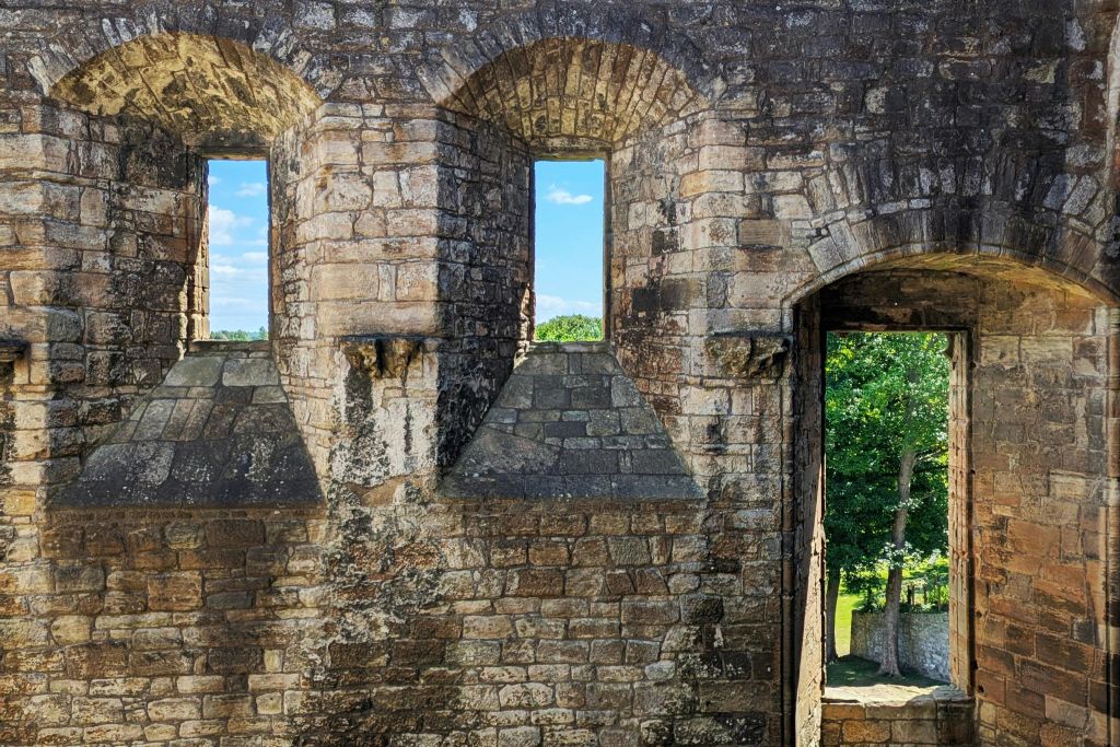 아치형 개구부가 있는 돌담은 푸른 풍경과 그 너머의 푸른 하늘을 보여줍니다.