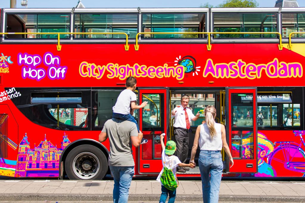 '암스테르담 시내 관광' 이라고 적힌 빨간색 2층 버스에 가족이 탑승하고 있으며, 기사님이 승객을 맞이합니다.