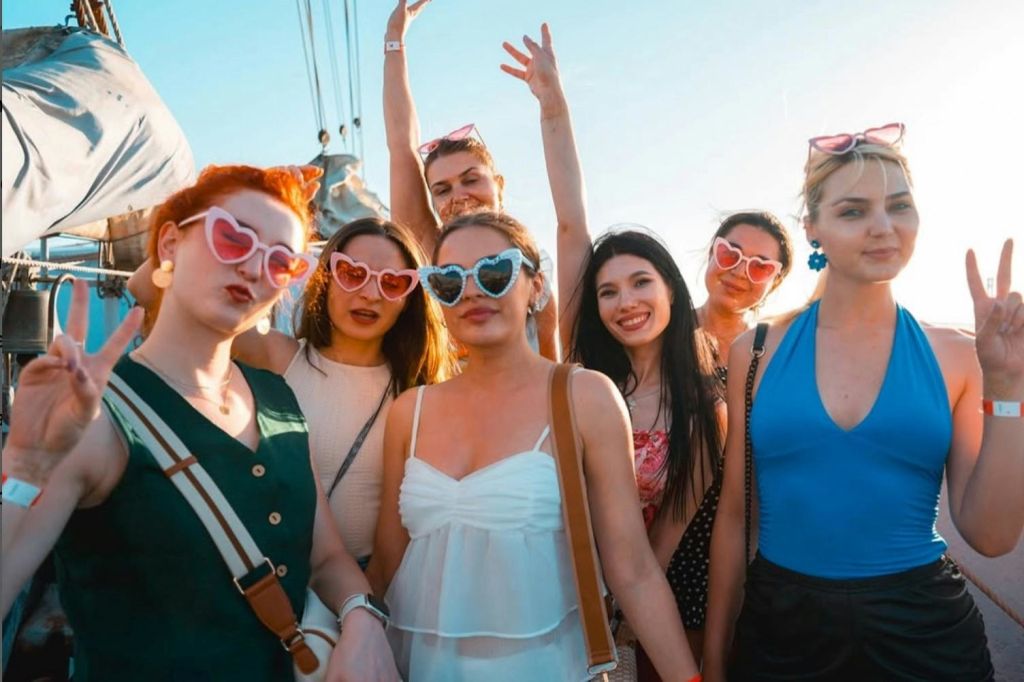 화려한 의상과 하트 모양의 선글라스를 착용하고 웃으며 화창한 날씨를 즐기는 야외 여성 그룹.