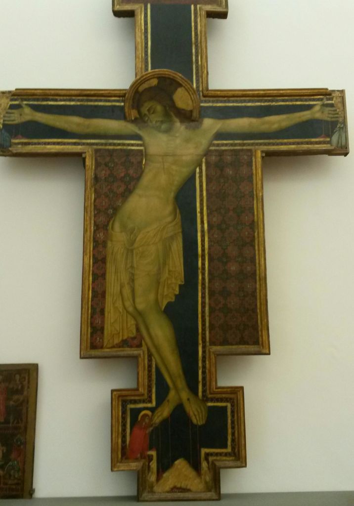 화려한 패턴의 배경에 세팅된 천으로 장식된 금빛 후광이 있는 예수님이 그려진 십자고상.