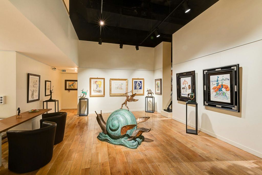 흰색 벽에 액자 그림이 있는 미술관, 나무 바닥, 검은 천장, 달팽이의 조각상, 사람의 모습이 중앙에 있습니다.