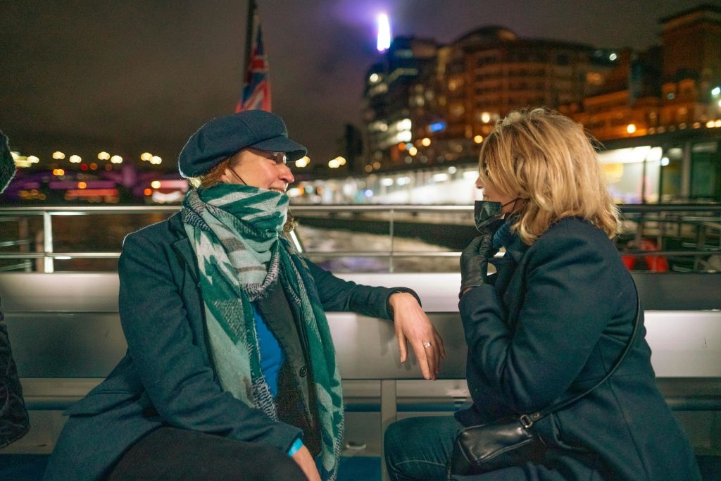 밤에 보트에 앉아 있는 두 사람, 한 사람은 스카프와 모자를 쓰고 도시 조명을 배경으로 앉아 있습니다.