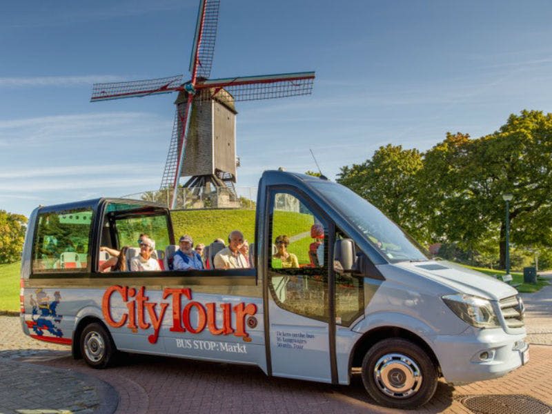 "시티투어" 브랜딩이 있는 투어 버스가 풍차 근처에 주차되어 있으며, 승객들이 앉고 녹지를 배경으로 운행됩니다.