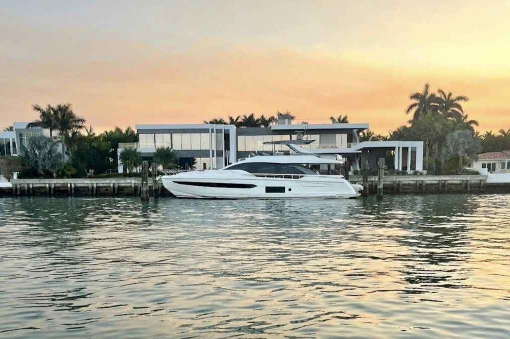파스텔 빛깔의 석양을 배경으로 현대적인 수변 주택 앞에 흰색 요트가 정박해 있습니다.