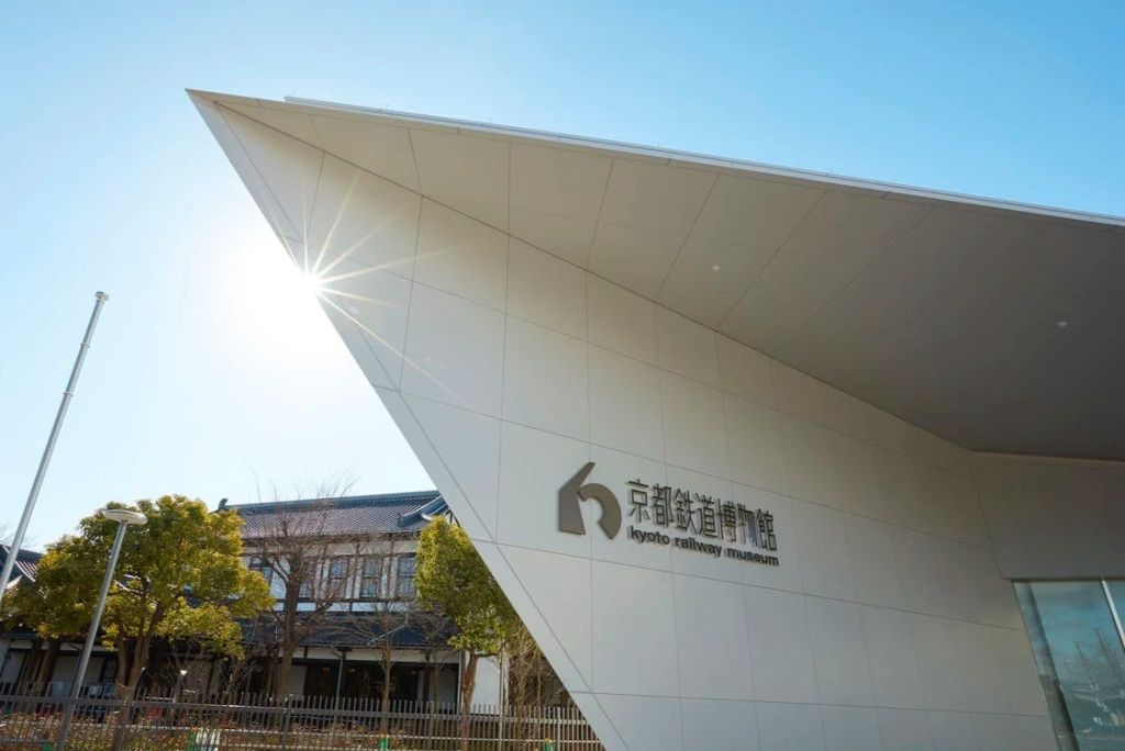 햇살이 내리쬐는 밝은 하늘 아래 '교토 철도 박물관' 간판이 영어와 일본어로 된 건물 코너.
