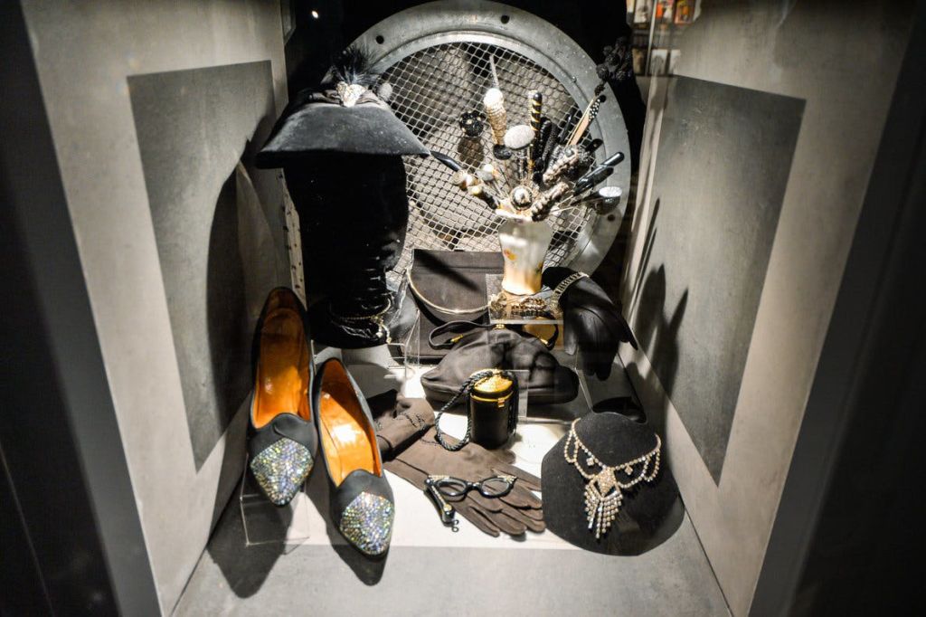 신발, 모자, 장갑, 목걸이, 손 모양의 보석 홀더 등 검은색 패션 액세서리가 들어간 진열 케이스.