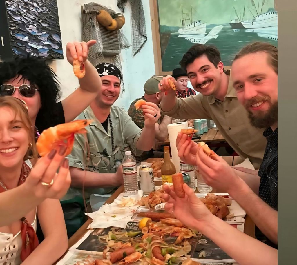 해산물 요리를 함께 즐기며 새우를 잡고 미소를 짓는 사람들의 모임으로, 해양을 테마로 한 배경이 있습니다.