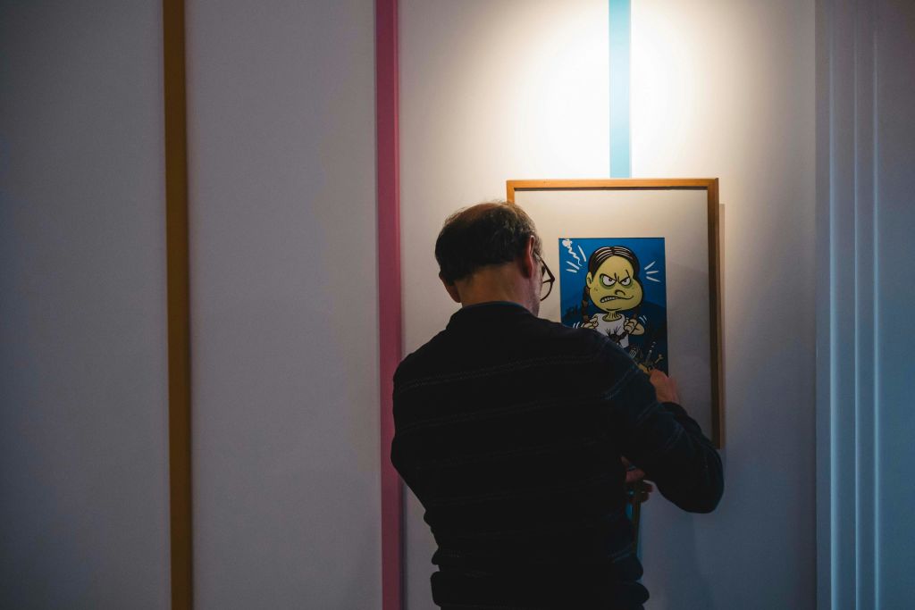한 사람이 액자에 담긴 만화 작품 앞에 서서 초점을 맞춘 조명 아래 흰색 벽을 조정하고 있습니다.