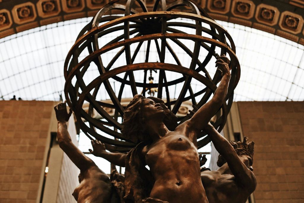 금속 지구본 구조로 둘러싸인 팔을 들어 올린 여성의 동상은 유리 지붕이 있는 건물에 보관되어 있습니다.