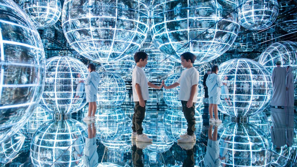 아이들은 미래 지향적이고 반사적인 공간에서 거울 표면과 커다란 빛나는 구체와 상호 작용합니다.