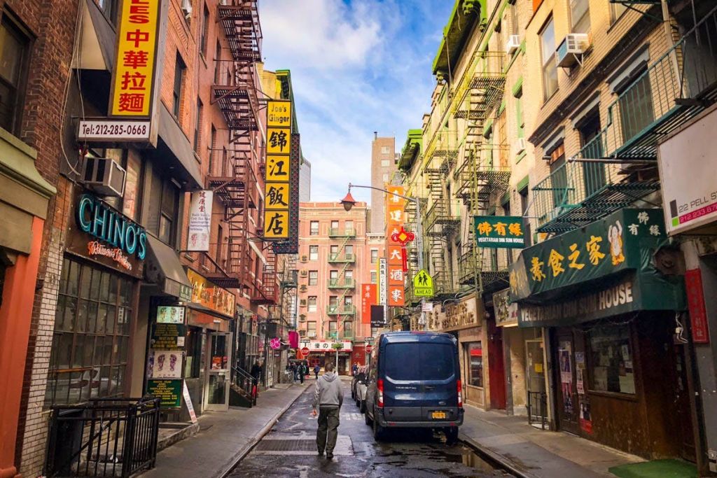 차이나타운의 좁은 거리에는 다채로운 간판, 화재 대피소, 상점, 블루 밴, 카메라를 피해 걸어가는 사람이 있습니다.