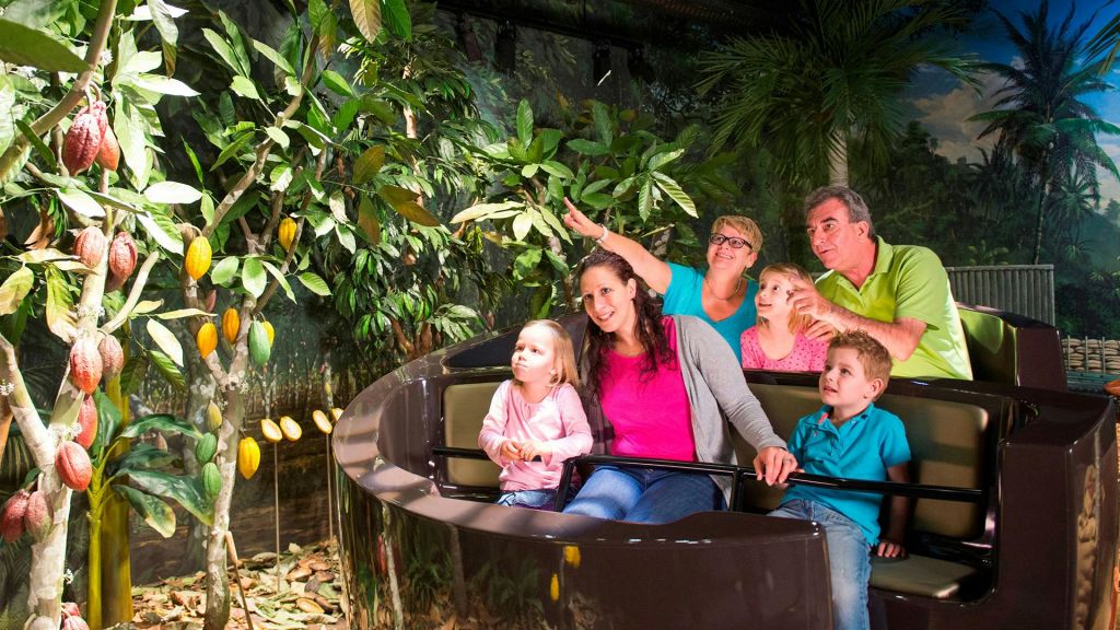 세 자녀를 포함한 여섯 명의 가족이 울창하고 정글 같은 초목으로 둘러싸인 놀이공원 보트를 타고 있습니다.