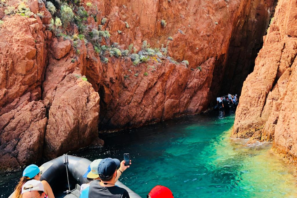 청록색의 맑은 물과 희박한 초목으로 덮인 바위 같은 질감의 벽이 있는 협곡에서 보트를 타는 사람들.