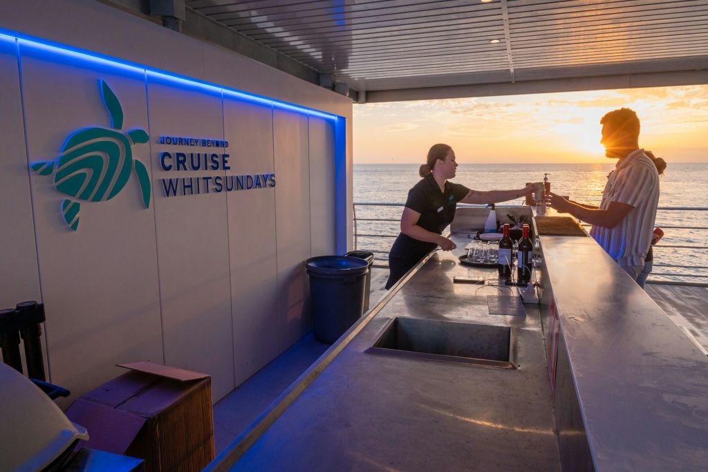 바다와 석양을 배경으로 한 현대적인 보트 바에서 바텐더가 고객에게 음료를 제공합니다.