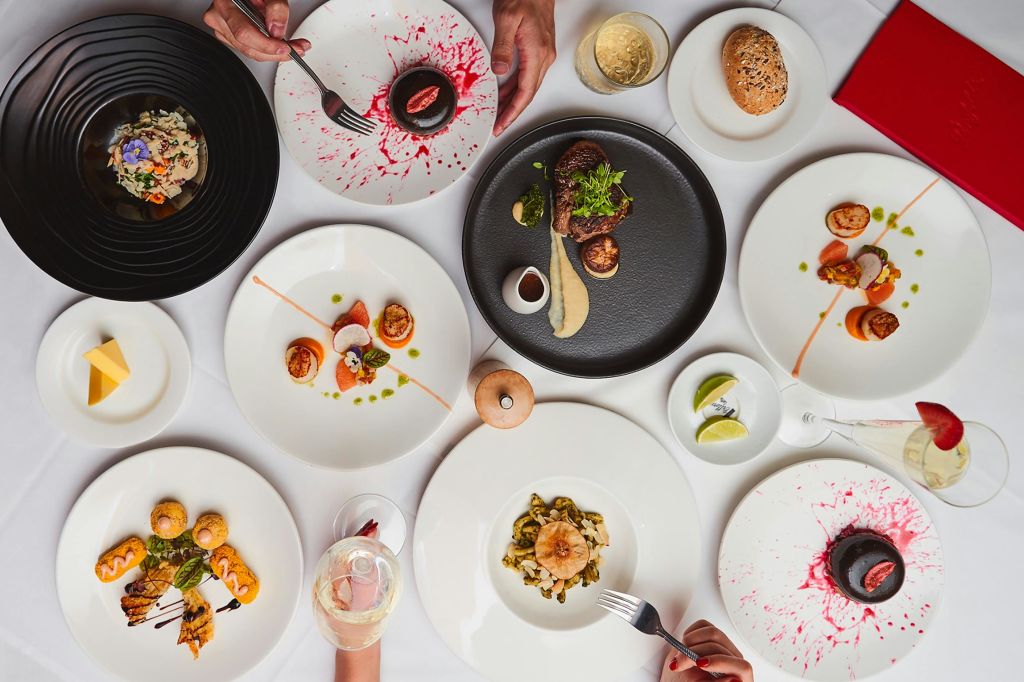 스테이크, 디저트, 장식된 애피타이저 등 6가지 고급 요리와 샴페인 2잔이 놓인 테이블입니다.