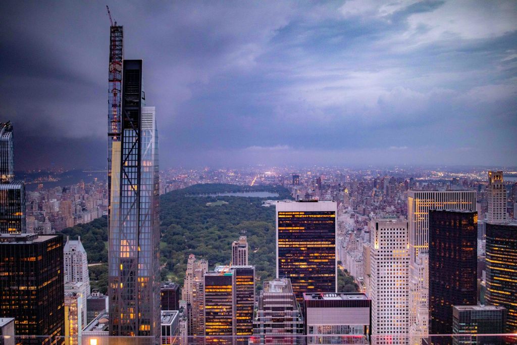 중앙 공원과 흐린 하늘 아래 밝게 빛나는 건물이 있는 해질 무렵의 도시 스카이라인.