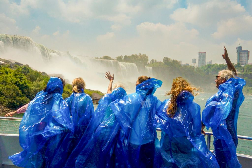 푸른 판초를 입고 뒤에서 바라보며 흐린 하늘 아래 커다란 폭포를 마주하고 있는 사람들의 무리.