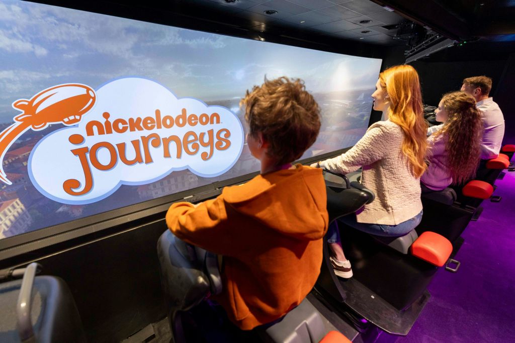 'Nickelodeon Journeys' 가 표시된 스크린 앞에 시뮬레이터 좌석에 앉아 있는 한 아이와 한 여성.