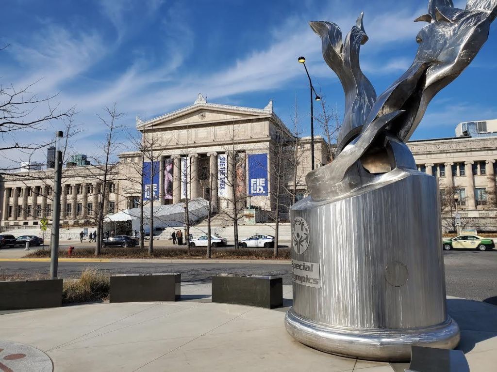 올림픽 특별 로고가 새겨진 금속 조각품으로, 역사적인 건물을 배경으로 하고 있습니다.