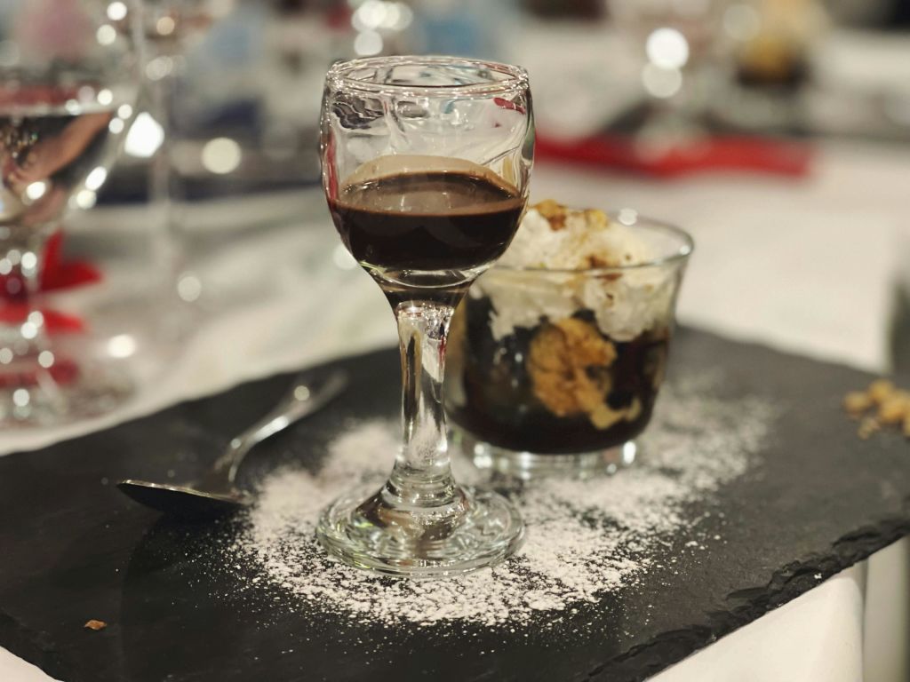 가루 설탕이 묻은 슬레이트 접시에 담긴 유리 접시에 진한 액체 잔과 디저트. 측면에 숟가락을 놓습니다.